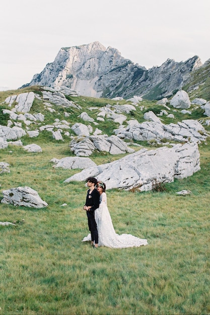 La novia y el novio están parados entre las enormes rocas grises.