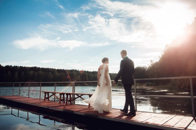 Novia y el novio están de pie en el puente en el lago. La pareja de recién casados