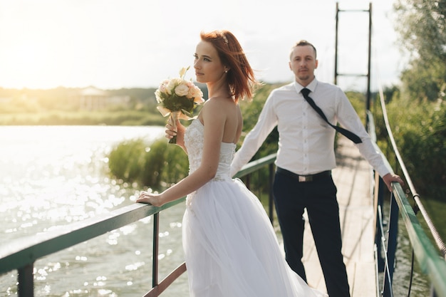 La novia y el novio están de pie en el puente