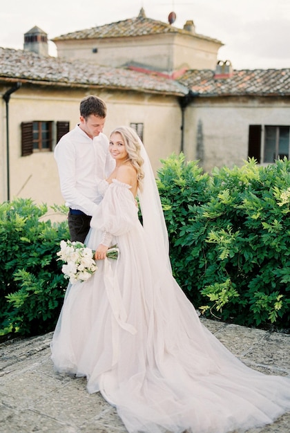 La novia y el novio están de pie en la terraza de una antigua villa cerca de los arbustos verdes florencia italia