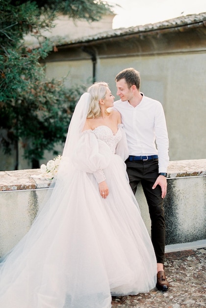 La novia y el novio están sentados en una valla de piedra en el jardín cerca de la antigua villa