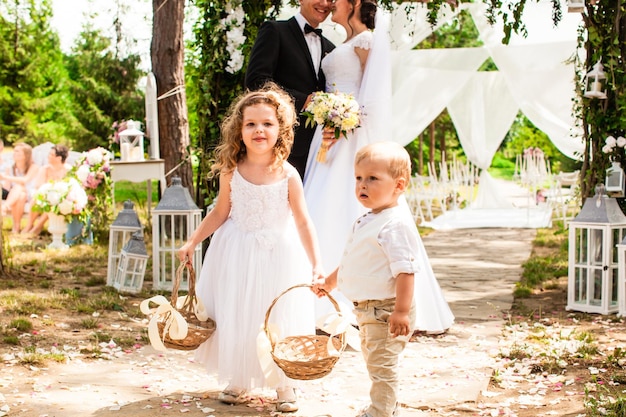 La novia y el novio están sonriendo después de la ceremonia de boda. Niños adorables con pétalos de rosa voladores en cestas.