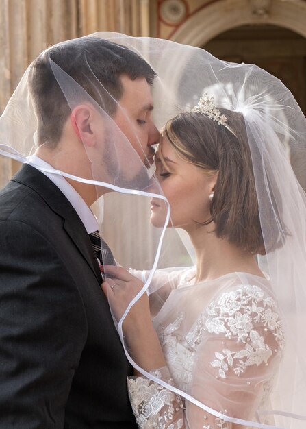 La novia y el novio felices se abrazan bajo el velo suave toque Boda