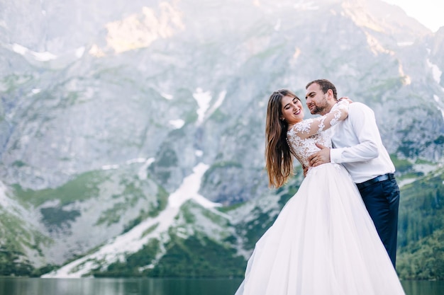 La novia y el novio junto al lago en las montañas Recién casados juntos