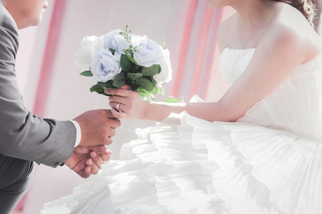 Novia y el novio de la mano y un ramo de flores hermosas