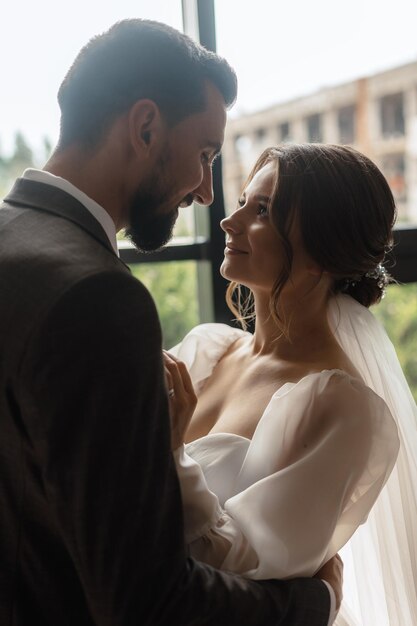 Novia y novio mirándose frente a una ventana