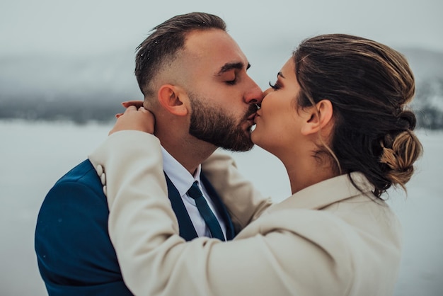 Novia y novio entre montañas nevadas Están de pie y abrazándose Boda de invierno al aire libre Cerrar