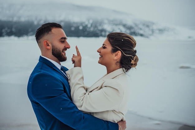 Novia y novio entre montañas nevadas Están de pie y abrazándose Boda de invierno al aire libre Cerrar