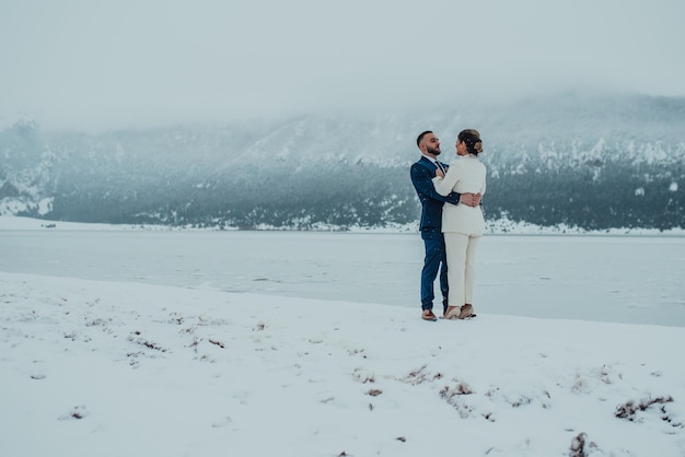 Novia y novio entre montañas nevadas Están de pie y abrazándose Boda de invierno al aire libre Cerrar