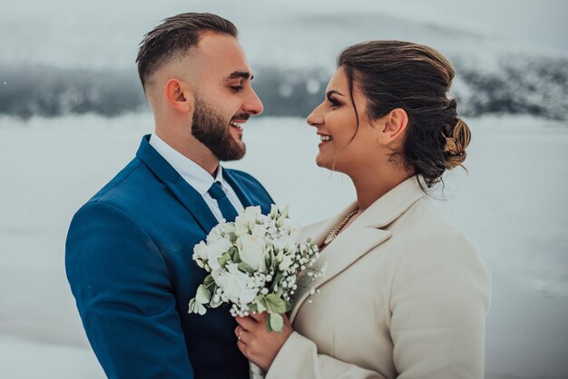 Novia y novio entre montañas nevadas Están de pie y abrazándose Boda de invierno al aire libre Cerrar