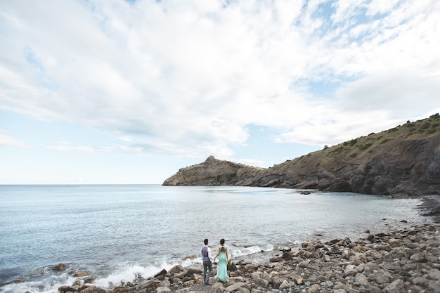 La novia y el novio en la naturaleza en las montañas cerca del agua