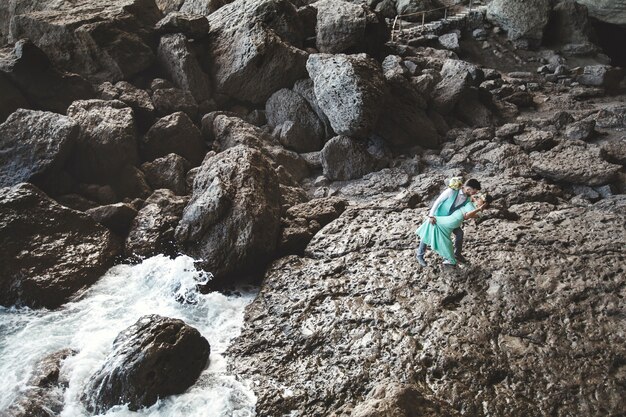 La novia y el novio en la naturaleza en las montañas cerca del agua.