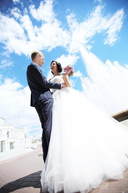 Novia y novio parados juntos bajo el cielo azul