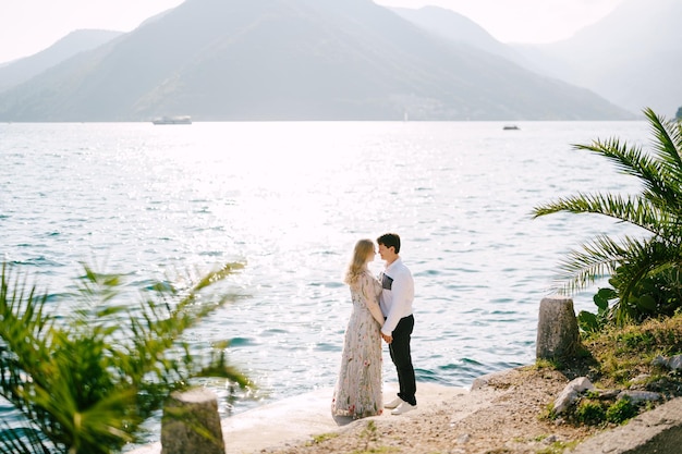 La novia y el novio se paran en la carretera perast con el telón de fondo de las montañas de montenegro