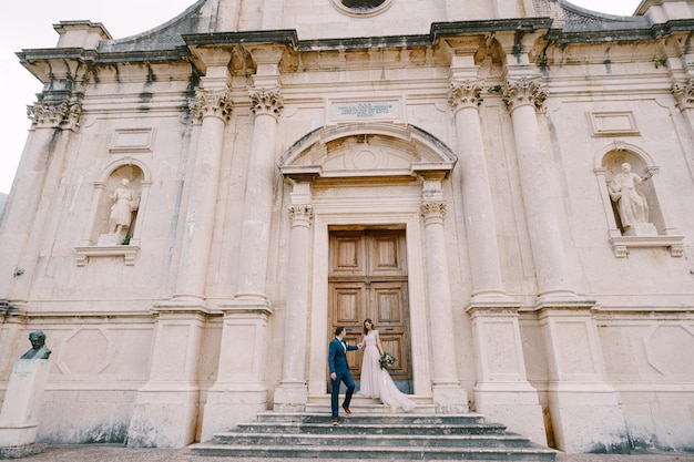 La novia y el novio se paran en los escalones de piedra de la antigua iglesia