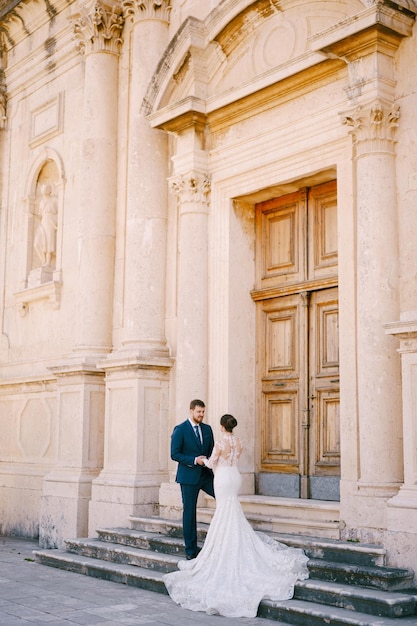 La novia y el novio se paran en los escalones de piedra frente a la puerta de madera de la antigua iglesia