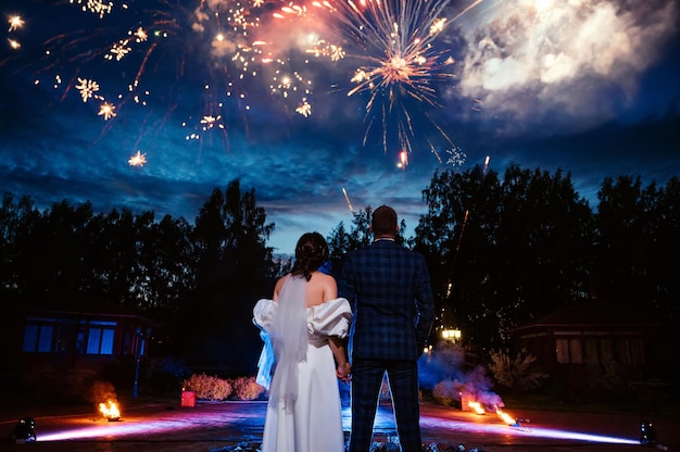 La novia y el novio se paran de espaldas contra el fondo de los fuegos artificiales festivos el día de la boda