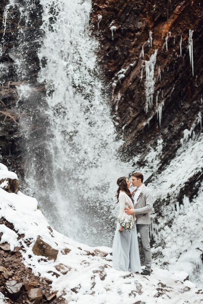 La novia y el novio en la pared de una cascada de montaña