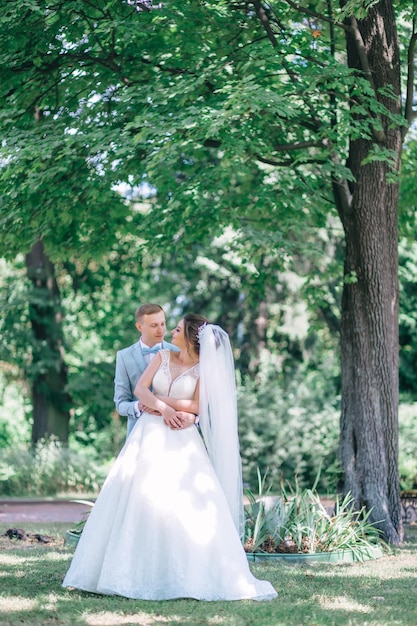 La novia y el novio de la pareja feliz se abrazan y se paran en un parque verde