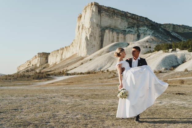 La novia y el novio de pie contra la gran roca blanca