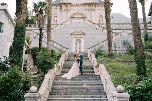 La novia y el novio de pie en los escalones del jardín de la iglesia en prcanj montenegro