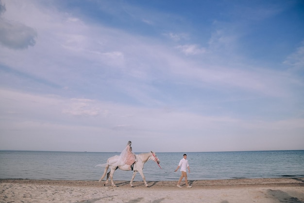 Novia y novio en la playa con caballos. Pareja de boda. Hermoso retrato en la naturaleza