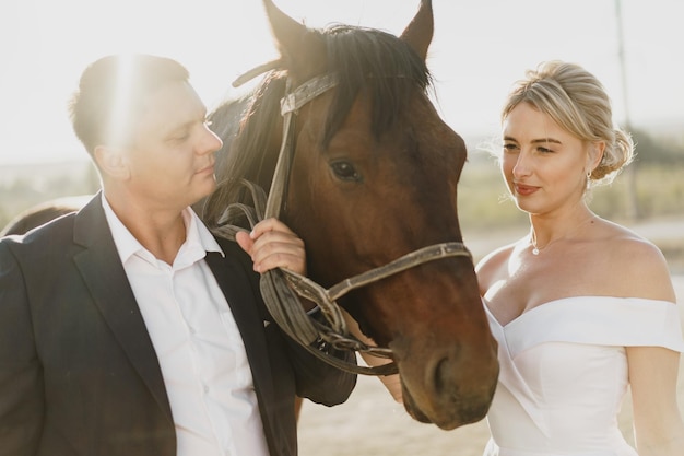 La novia y el novio posando con un caballo al atardecer