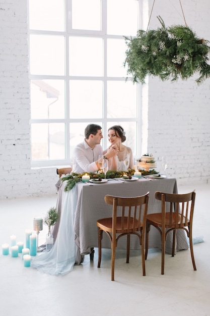 Novia y el novio posando en la mesa decorada en el salón blanco