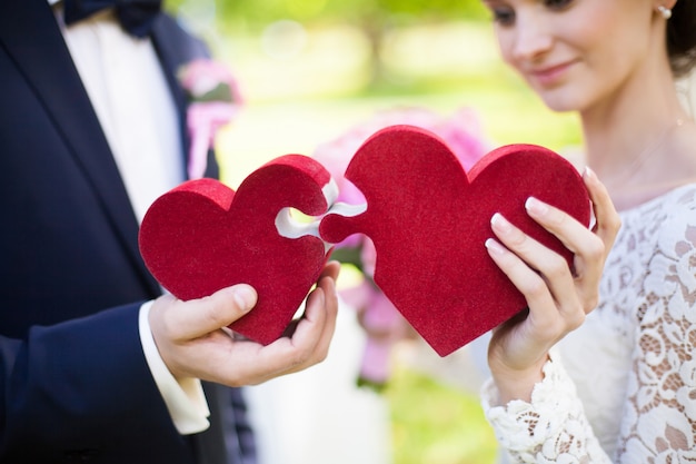 Foto novia y novio que llevan a cabo corazones rojos del rompecabezas, concepto de la boda, primer