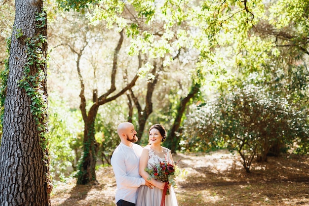 La novia y el novio con un ramo de flores se abrazan entre los árboles en un olivar