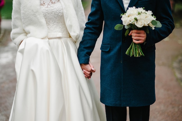 La novia y el novio con un ramo de novia tomados de la mano y de pie en la ceremonia de boda al aire libre en la naturaleza