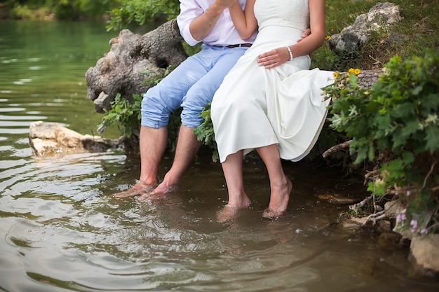 La novia y el novio sentados en la orilla del lago.