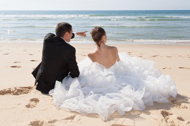 Novia y novio sentados en la playa