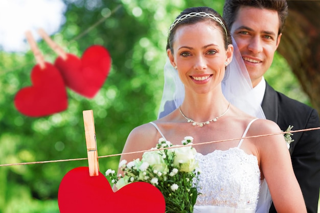 La novia y el novio sonrientes en el jardín contra corazones colgando de una línea