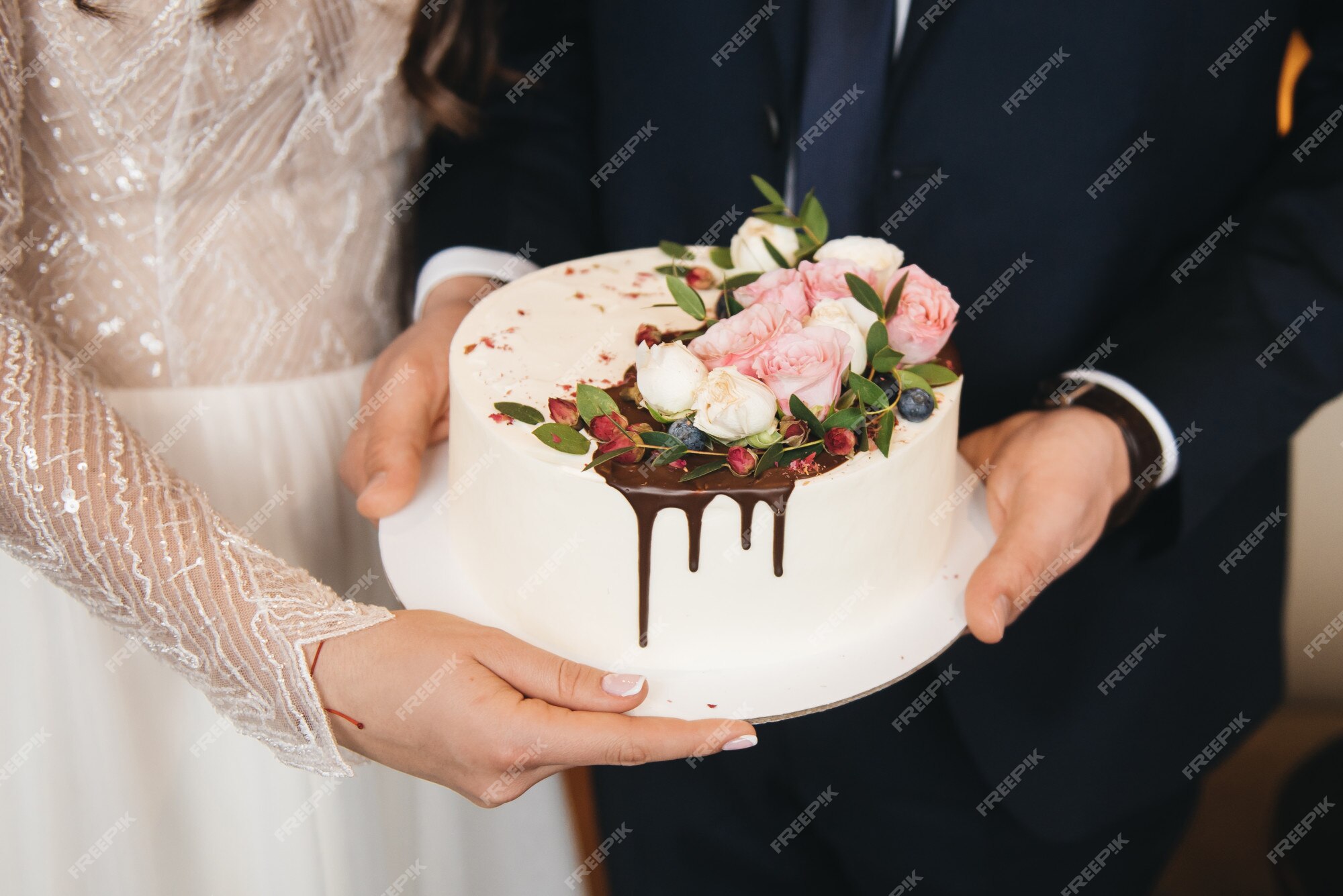 La novia y el novio sostienen un pequeño pastel de bodas decorado con  chocolate y flores. | Foto Premium