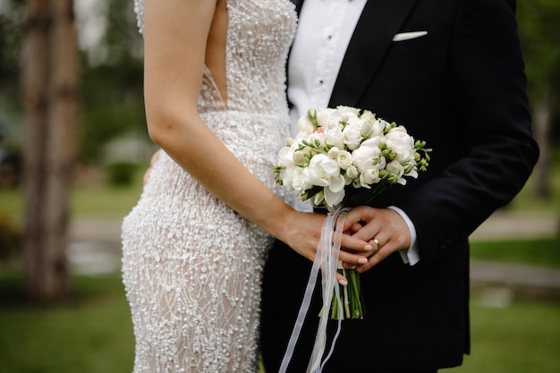 Una novia y un novio sostienen sus ramos de flores frente a un muro de piedra.