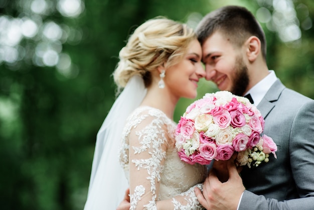 Novia y el novio en traje gris ven hermosa posando en un bosque de verano brillante