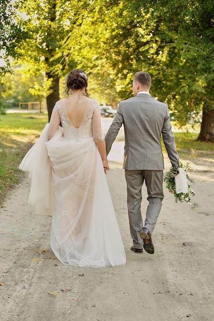 La novia y el novio van a casa a lo largo del camino a lo largo del campo verde