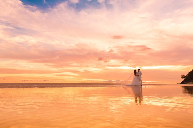 La novia y el novio con velo largo en la playa tropical al atardecer Boda y luna de miel en los trópicos