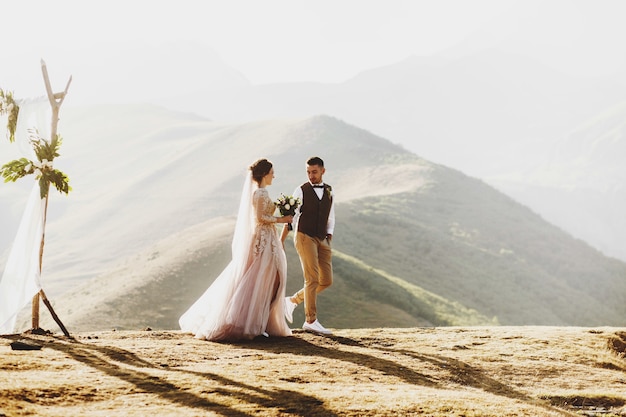 La novia y el novio se ven hermosos durante la ceremonia de la boda en la cima de la montaña en algún lugar de Georgia