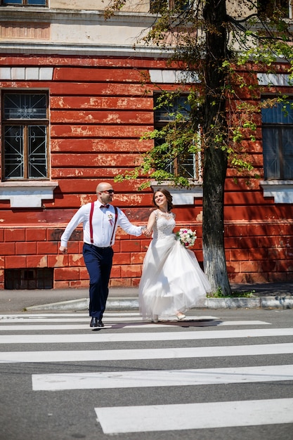 La novia y el novio en vestidos de novia caminando por las calles de la ciudad el día de la boda