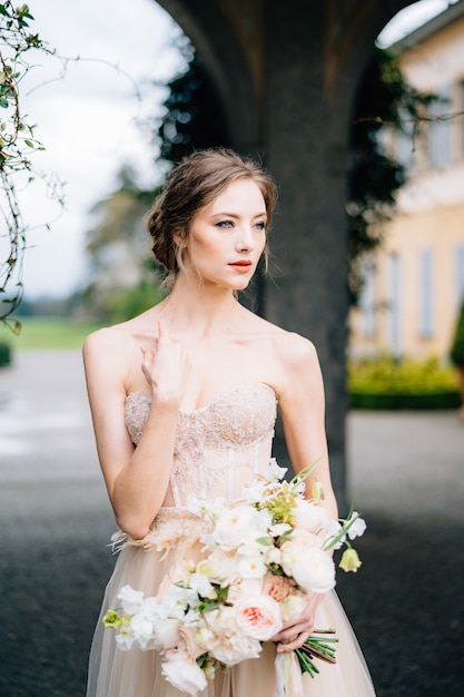 Novia pensativa con un vestido rosa tiene un ramo de flores en sus manos