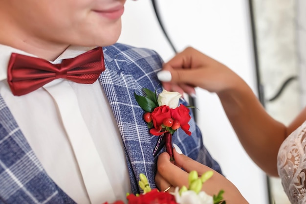 La novia pone al novio en el boutonniere de rosas rojas el día de la boda