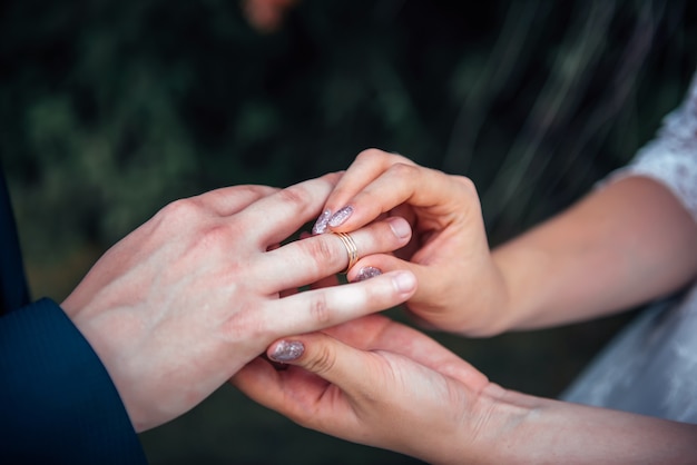 Novia poniendo el anillo de bodas de oro en el dedo del novio durante la ceremonia de la boda, de cerca.