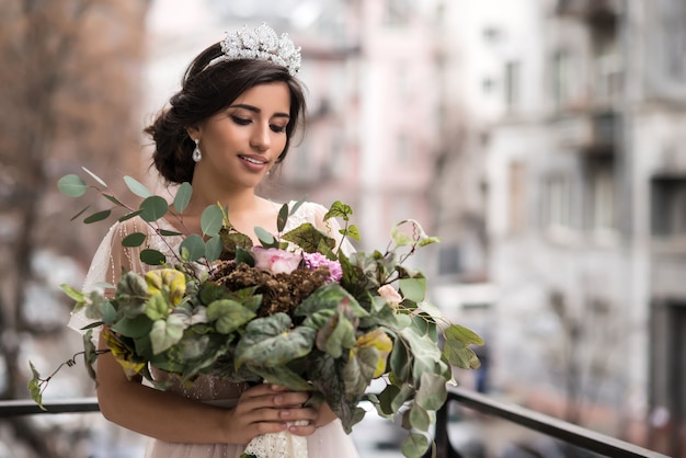 Novia con un ramo de flores en el balcón entre las calles de la gran ciudad.