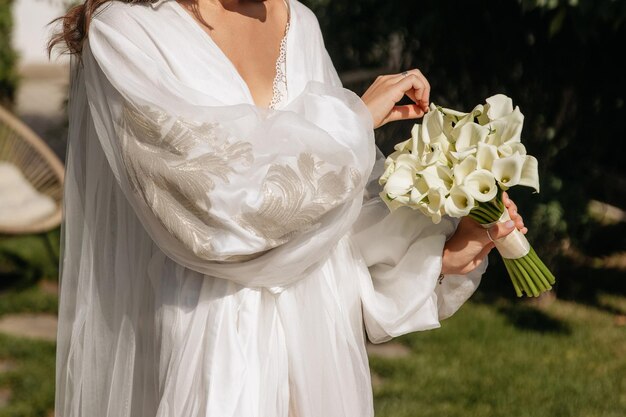 Foto la novia con un ramo de lirios blancos de calla está de pie en una luxuosa falda afuera en el sol