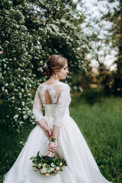 Novia con un ramo de novia en el bosque cerca de los arbustos con flores blancas