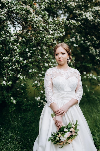 Novia con un ramo de novia en el bosque cerca de los arbustos con flores blancas