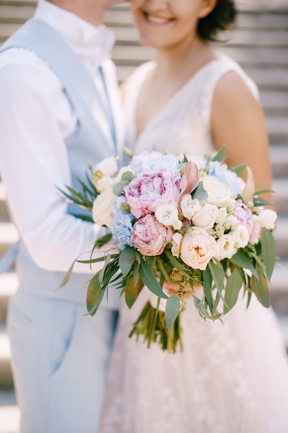 La novia con el ramo de rosas y peonías y el novio abrazándose en las antiguas escaleras en