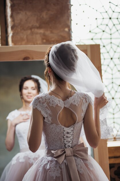 La novia se reúne en la mañana cerca del espejo y se ajusta el cabello.